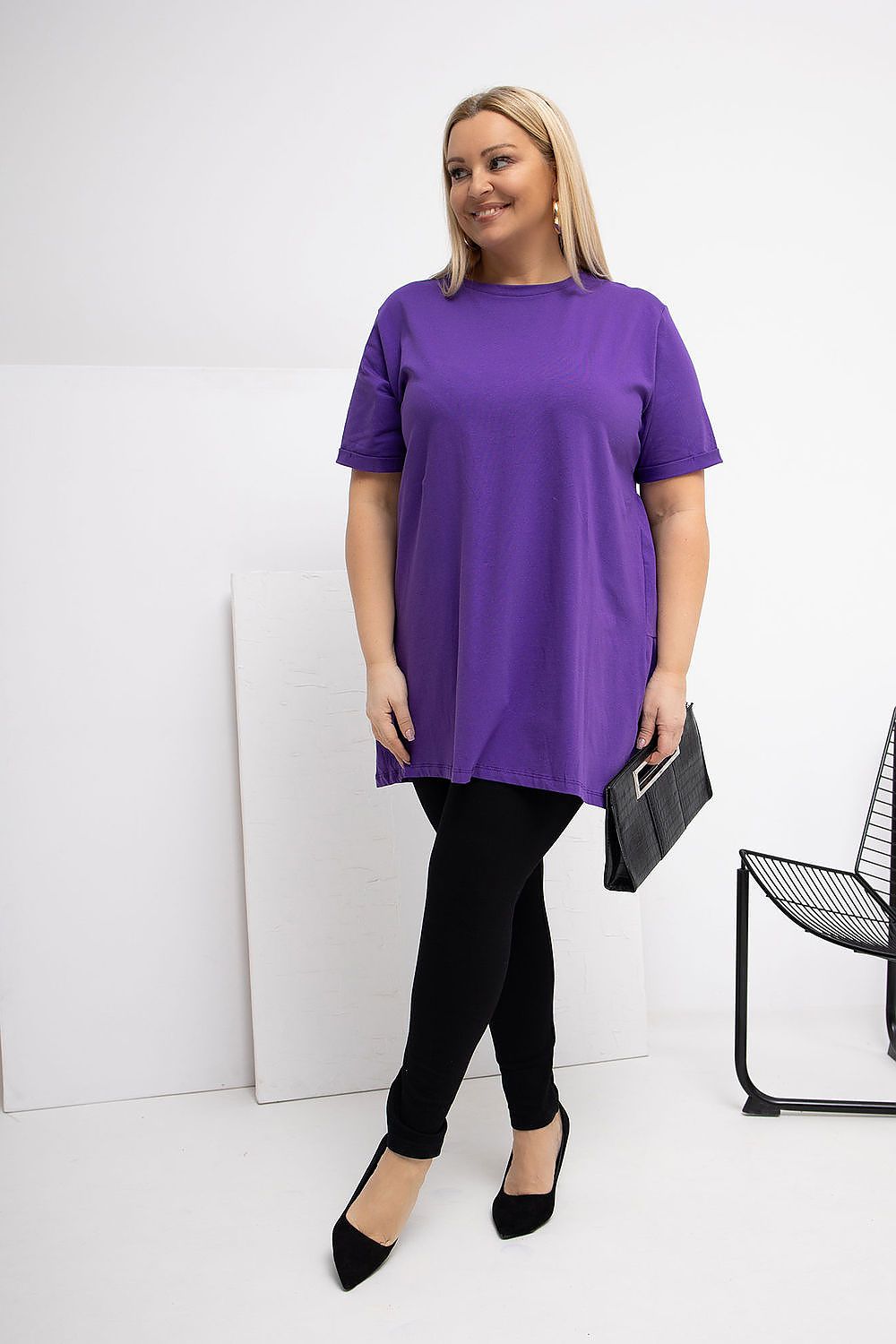 Woman wearing a purple tunic and black pants against a white background