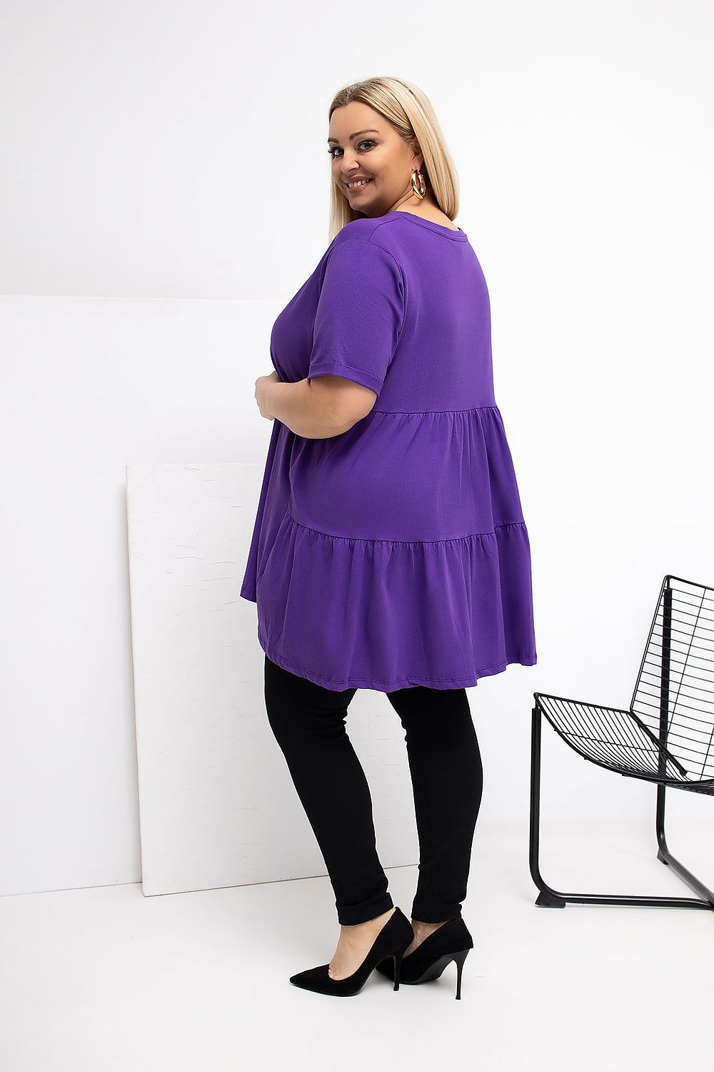 Woman wearing a purple dress and black pants against a white background