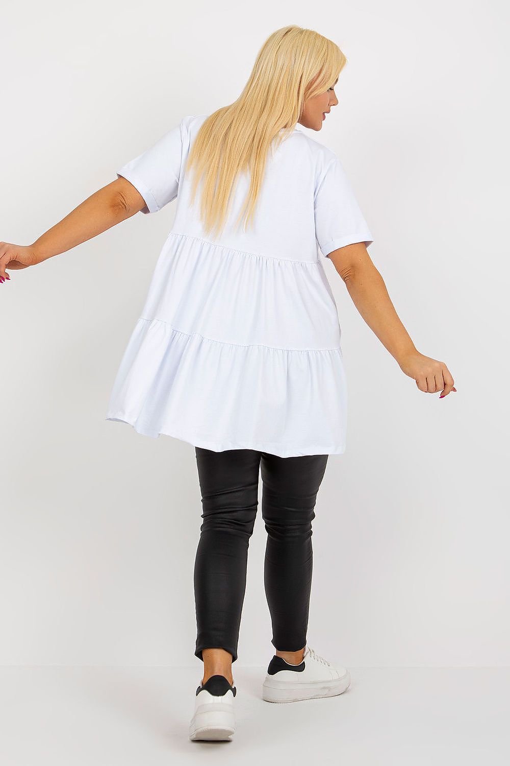 Person wearing a white tunic over black pants on a plain background