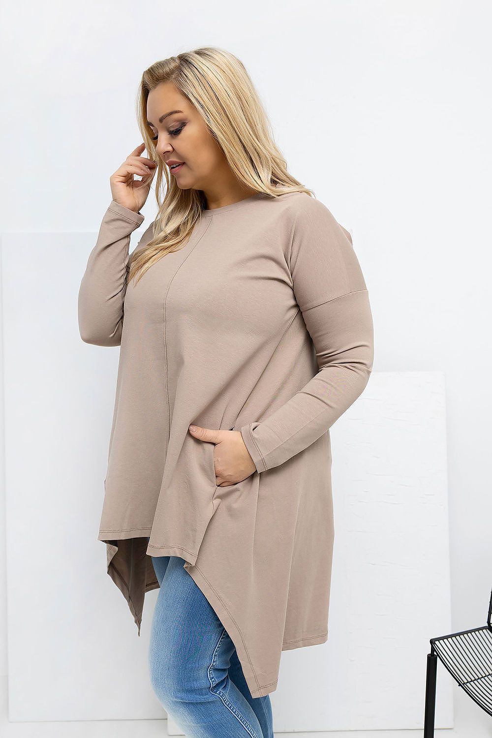 Woman wearing a long beige cardigan over blue jeans against a white background
