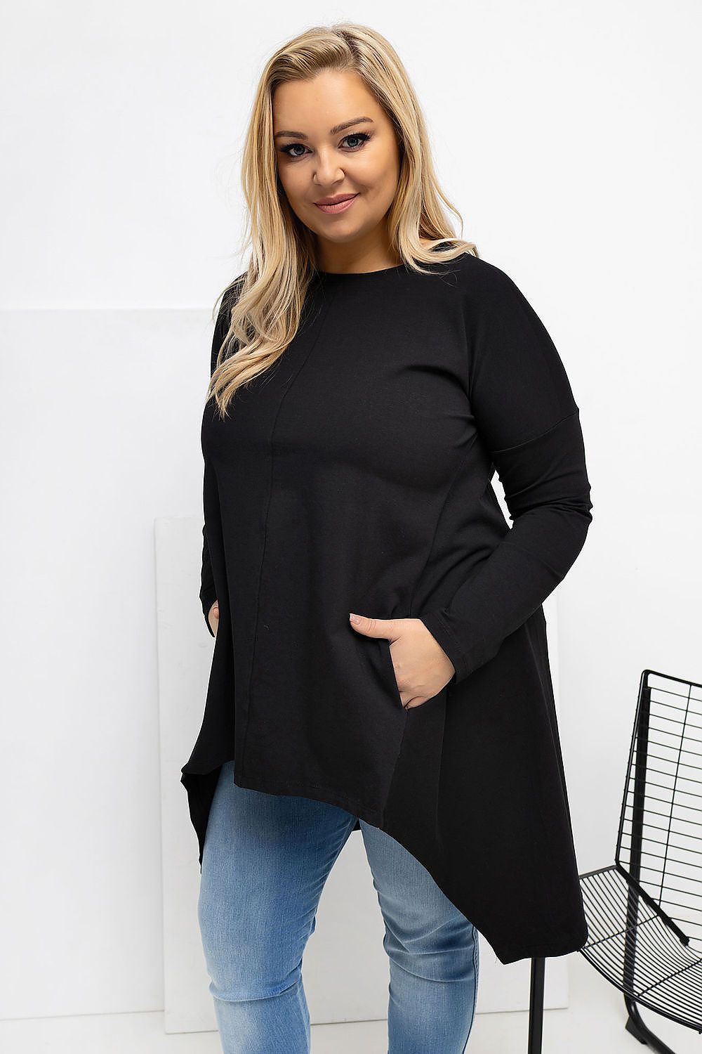 Woman wearing a black long-sleeve top and blue jeans against a white background