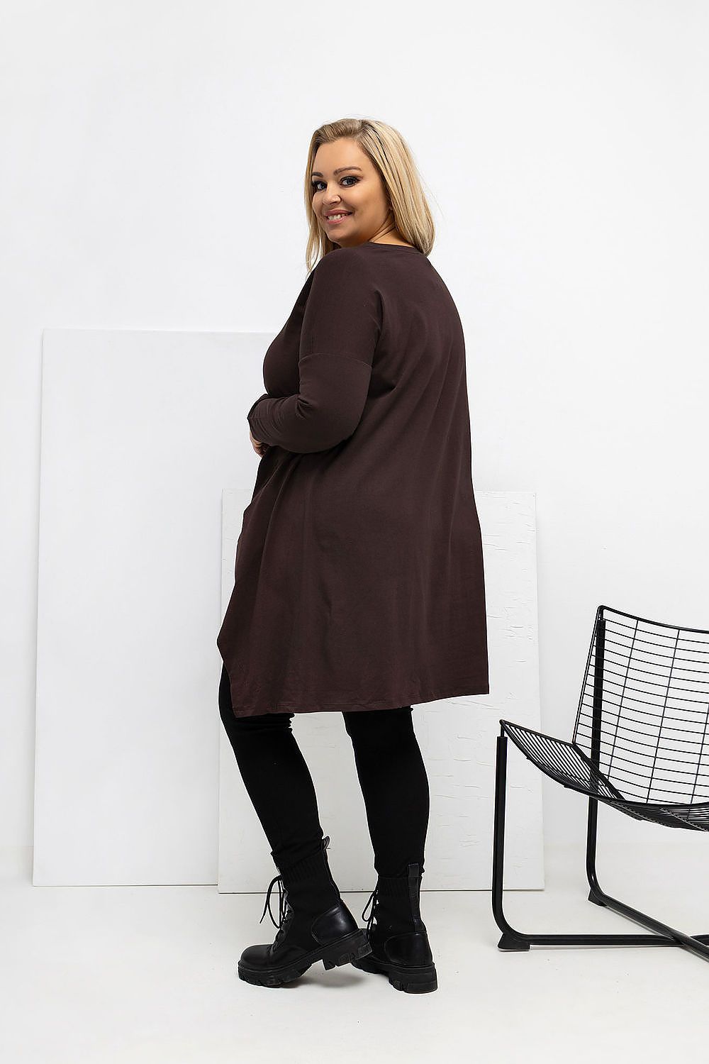 Woman wearing a brown dress with black tights and shoes in a minimalistic setting.