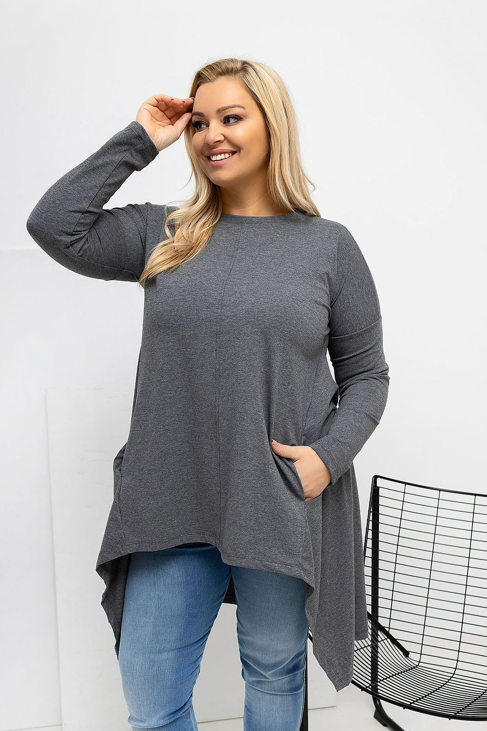 Woman wearing a gray long-sleeve top and blue jeans against a white background