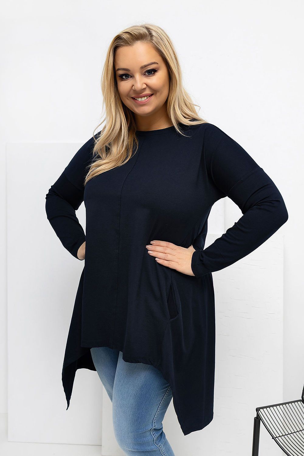 Woman wearing a black long-sleeve top and blue jeans against a white background