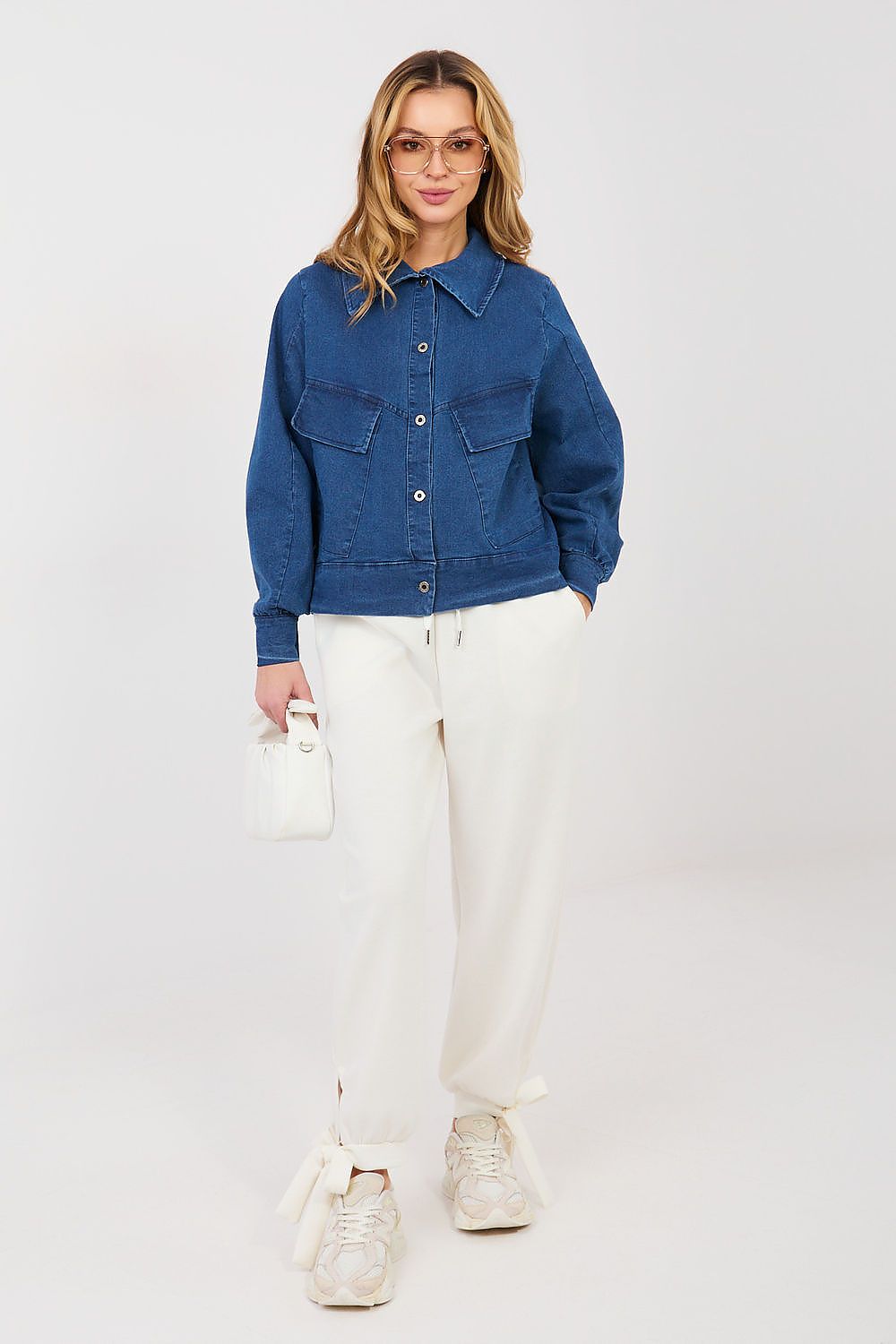 Woman wearing a blue denim jacket and white pants on a plain background