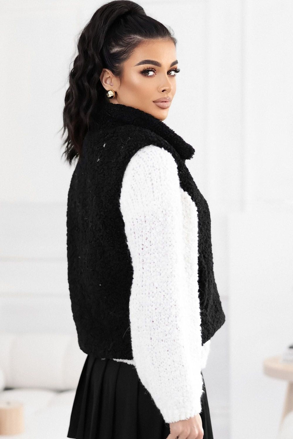 Woman wearing a black and white outfit with a textured black vest over a white long-sleeve top.