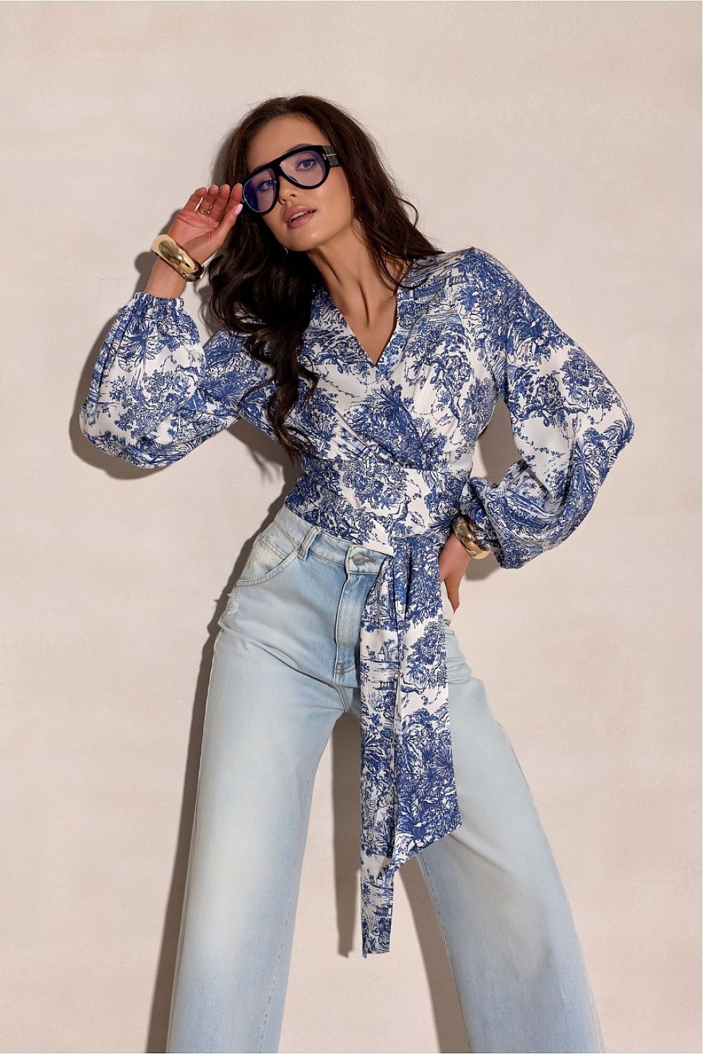 Woman wearing a blue floral blouse and light blue jeans against a beige background