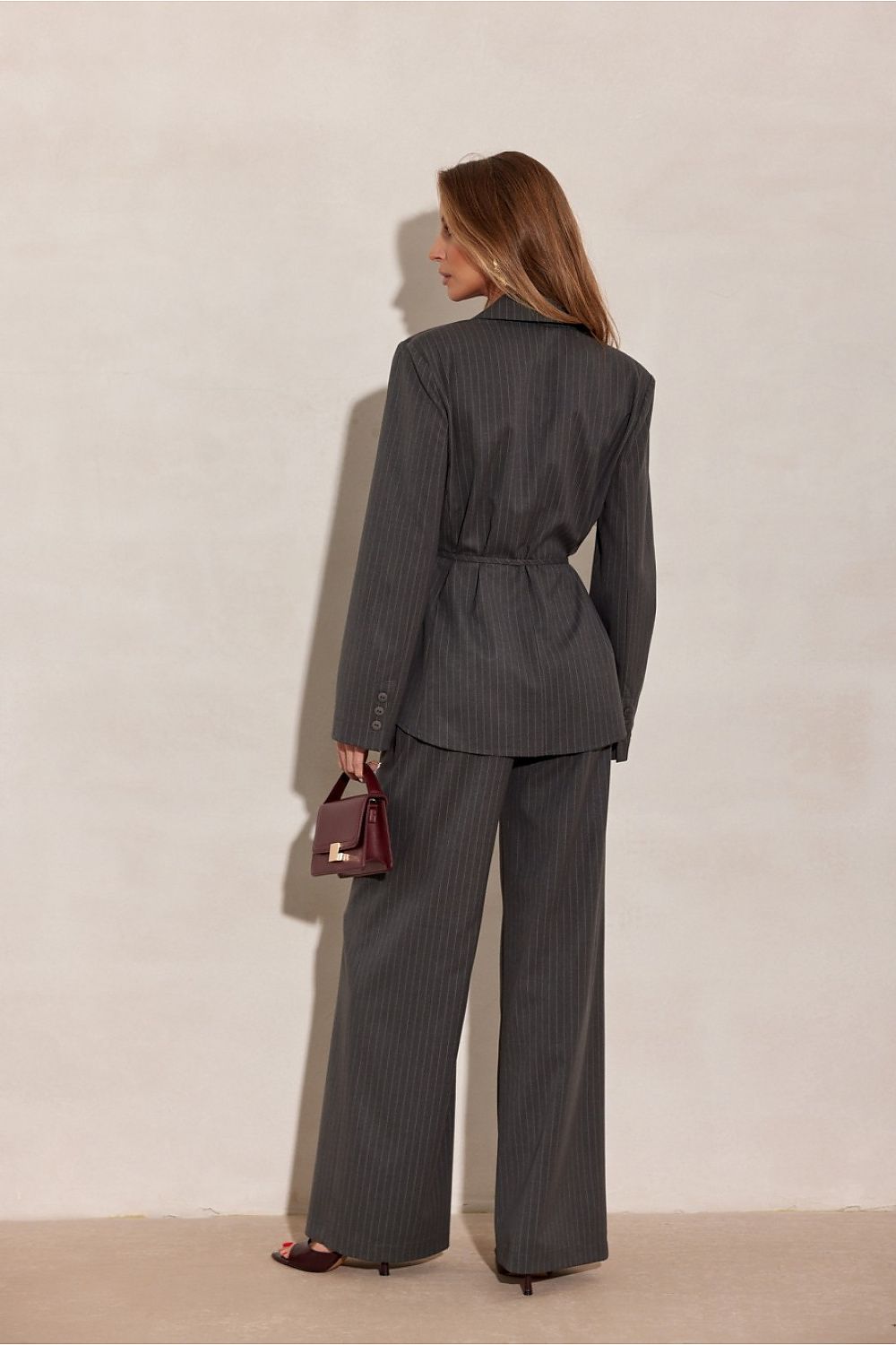 Woman wearing a grey pinstripe suit with a red handbag against a beige background