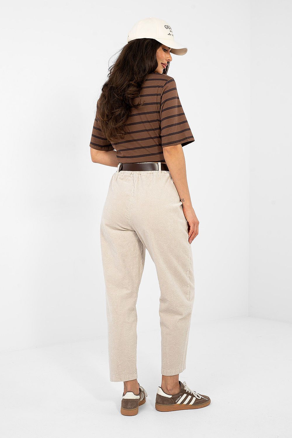 Woman wearing a striped shirt, beige pants, and a cap on a white background
