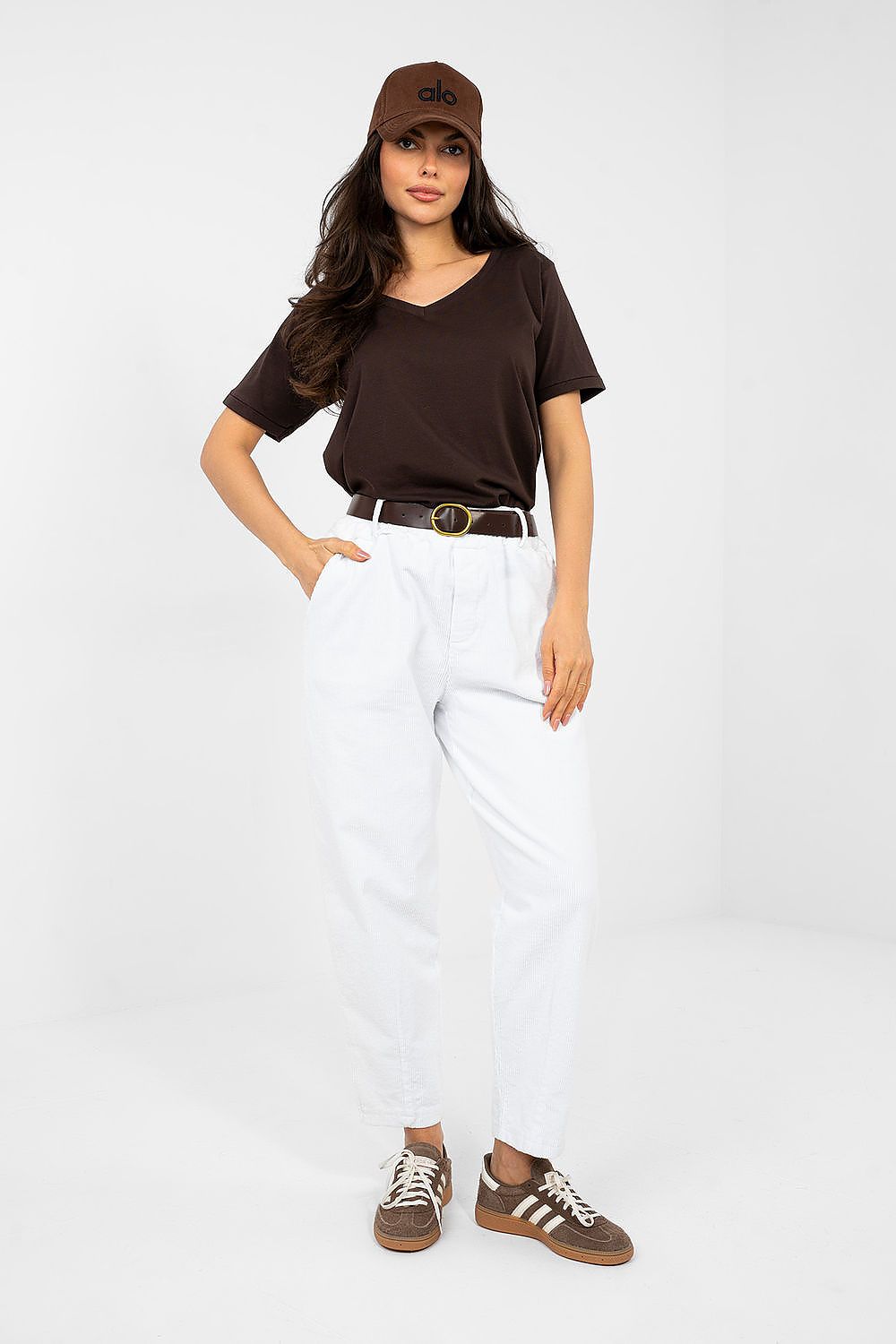 Woman wearing a brown t-shirt, white pants, and a brown cap on a white background