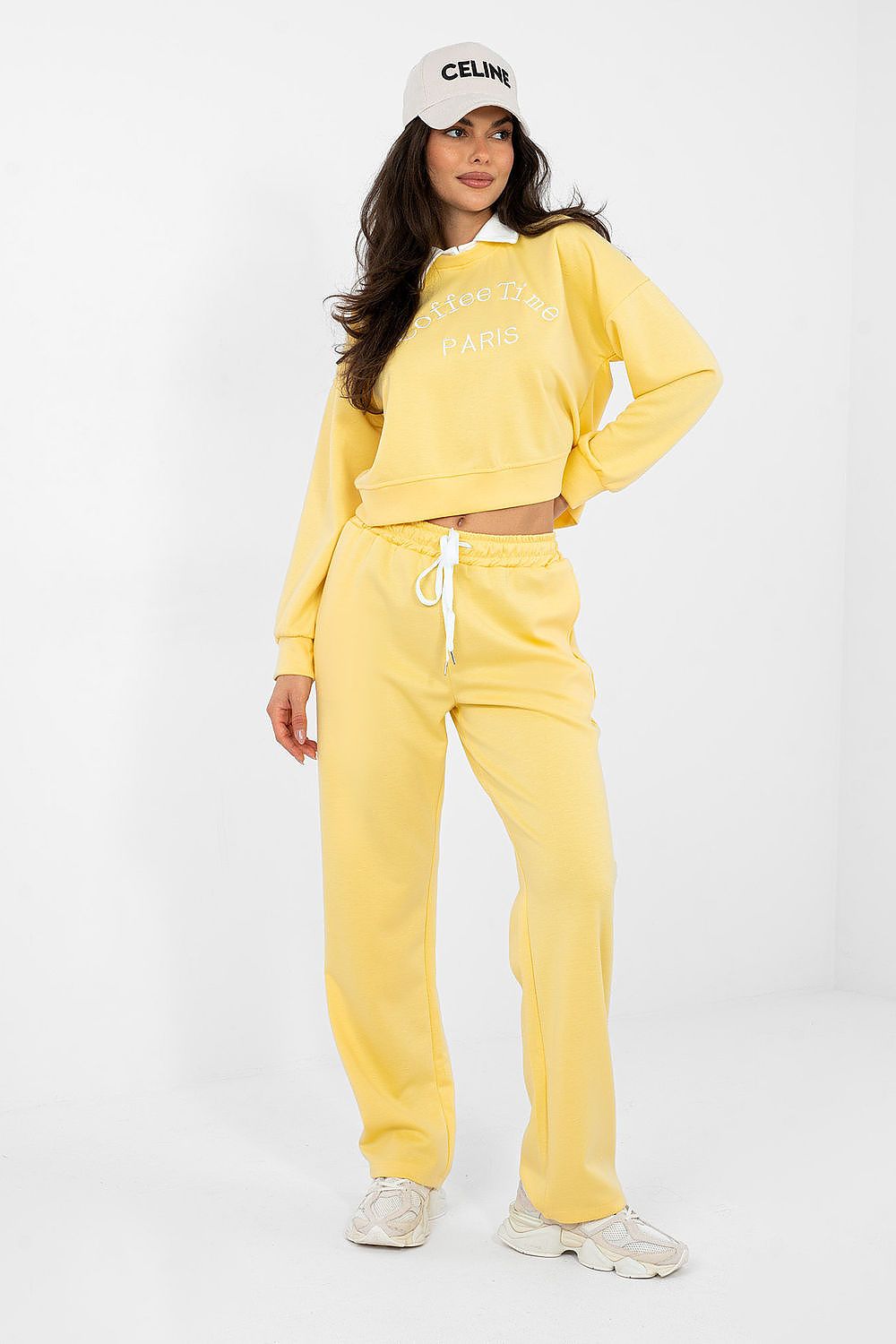 Woman wearing a yellow tracksuit with a white cap on a white background