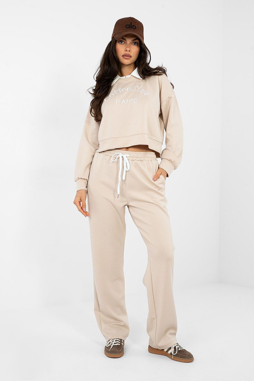 Woman wearing a beige tracksuit and brown cap on a white background