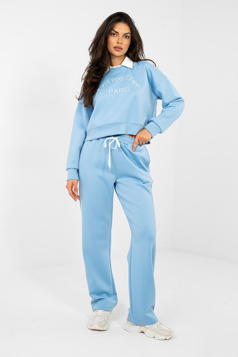 Woman wearing a light blue tracksuit with a white collar on a white background