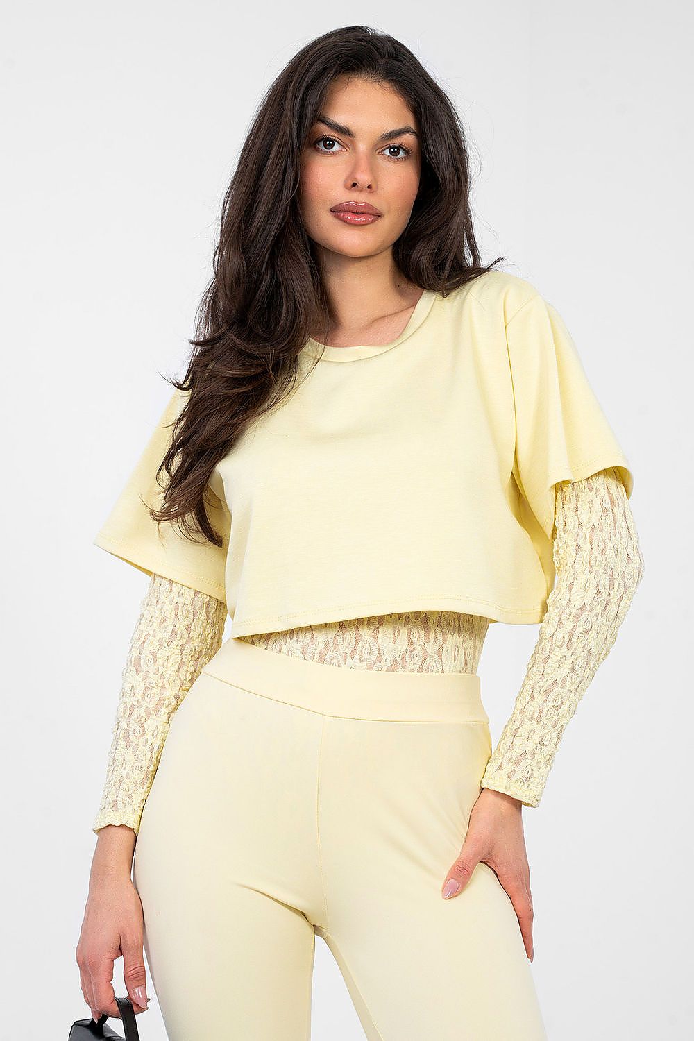 Woman wearing a light yellow outfit with a textured long-sleeve top and pants on a white background
