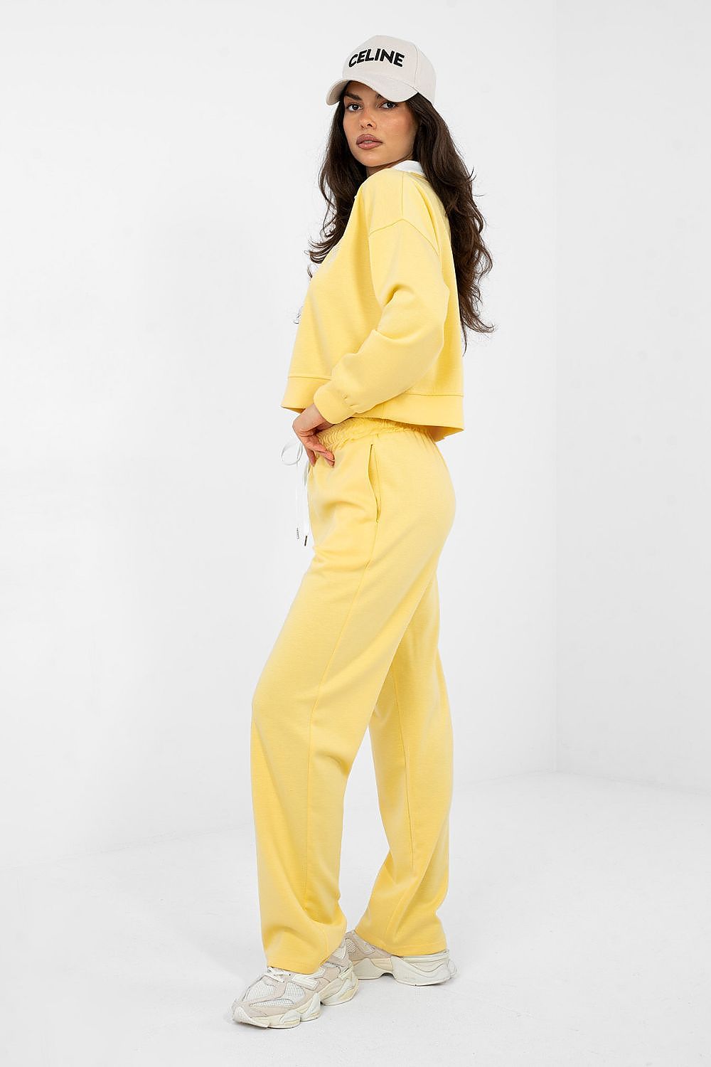 Person wearing a yellow tracksuit and white Celine cap on a white background