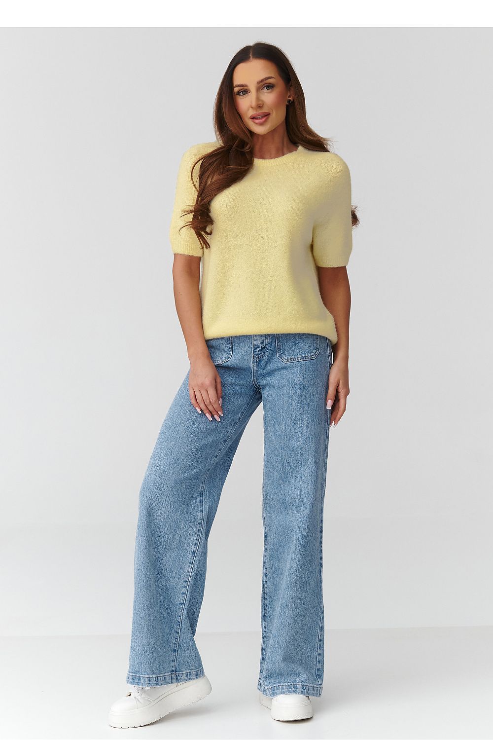 Woman wearing a yellow sweater and blue jeans on a white background