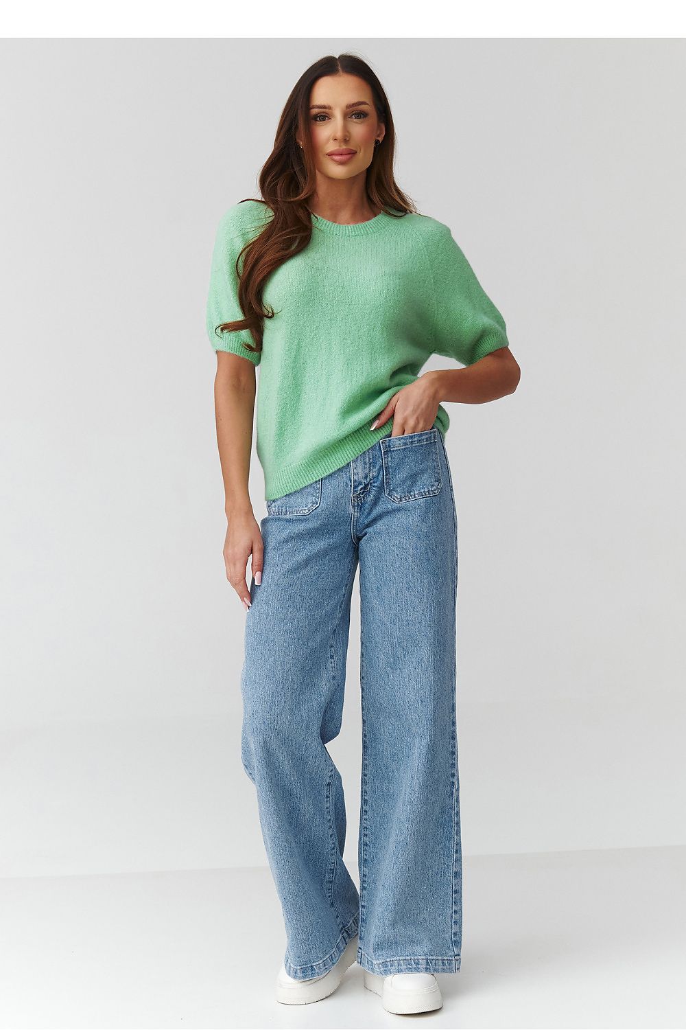 Woman wearing a green top and blue jeans on a white background
