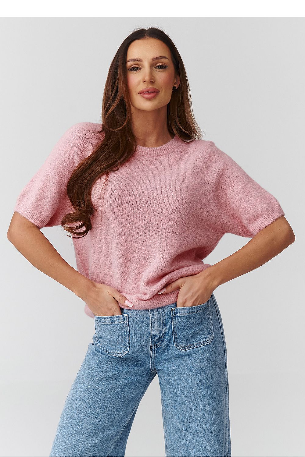 Woman wearing a pink sweater and blue jeans against a plain background