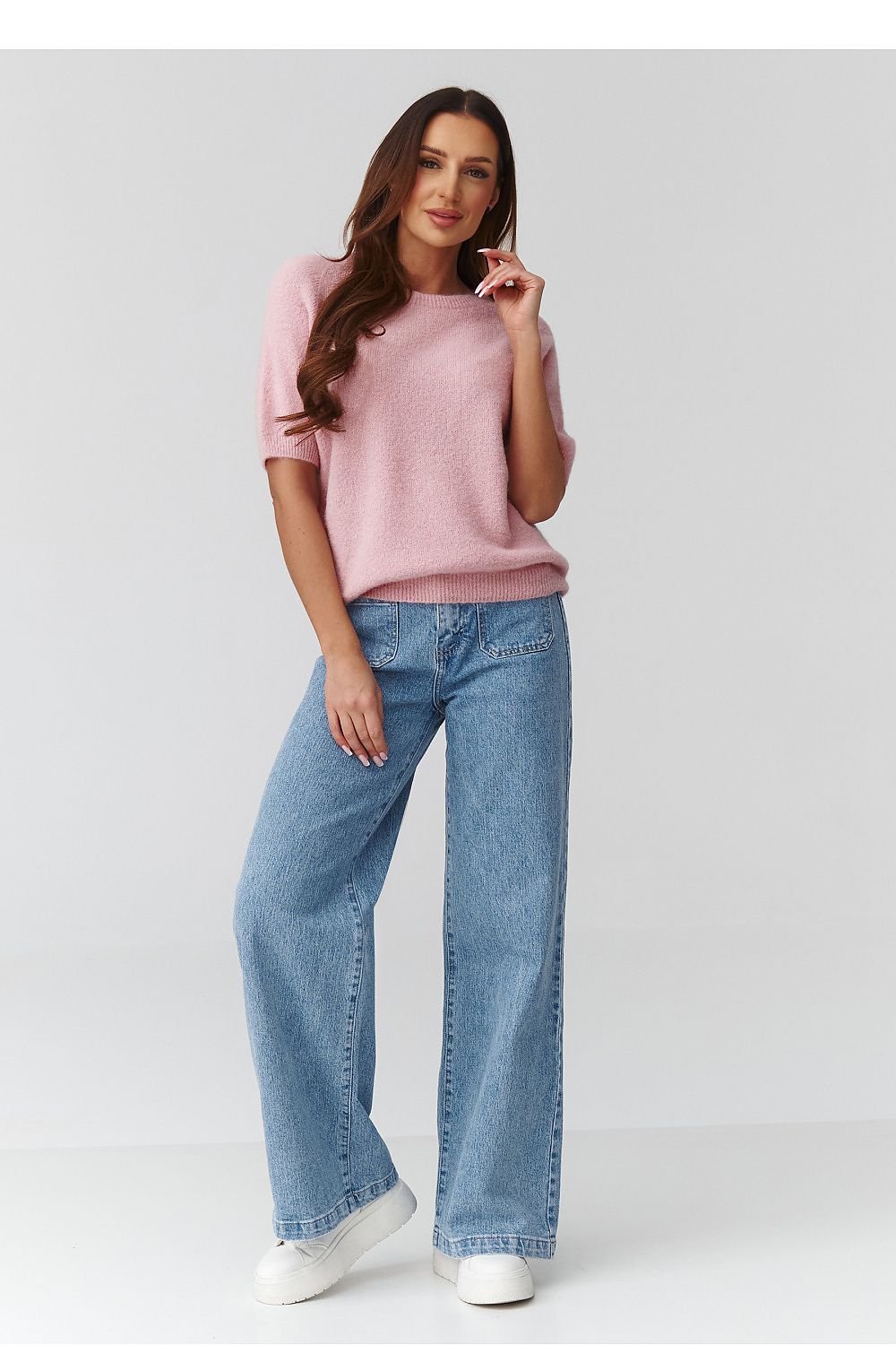 Woman wearing a pink sweater and blue jeans on a white background