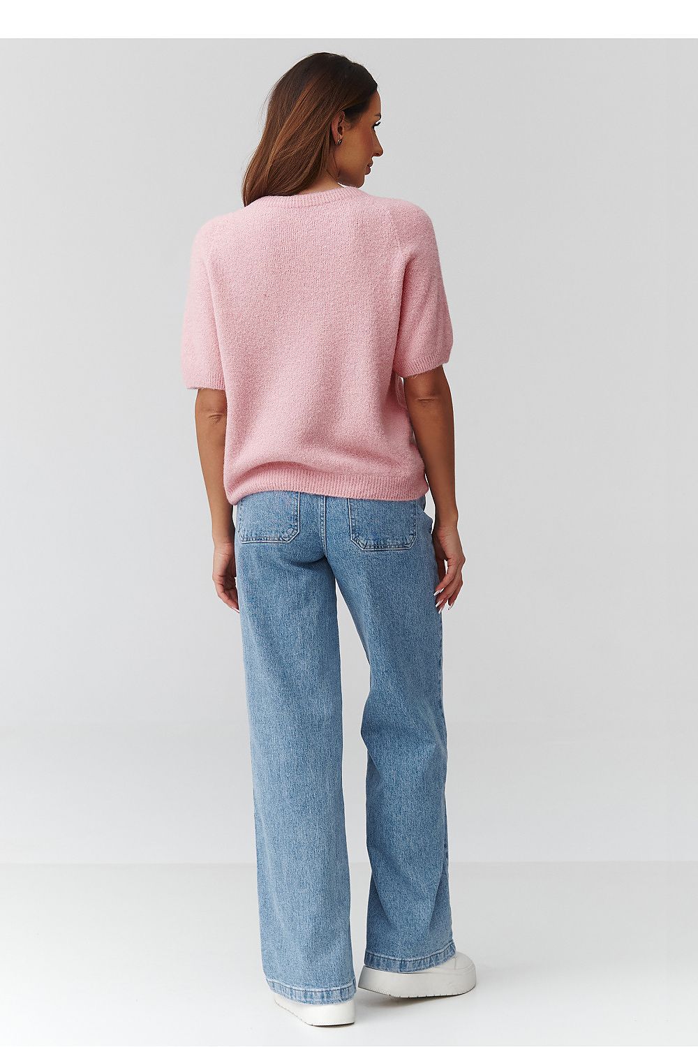 Person wearing a pink sweater and blue jeans on a white background