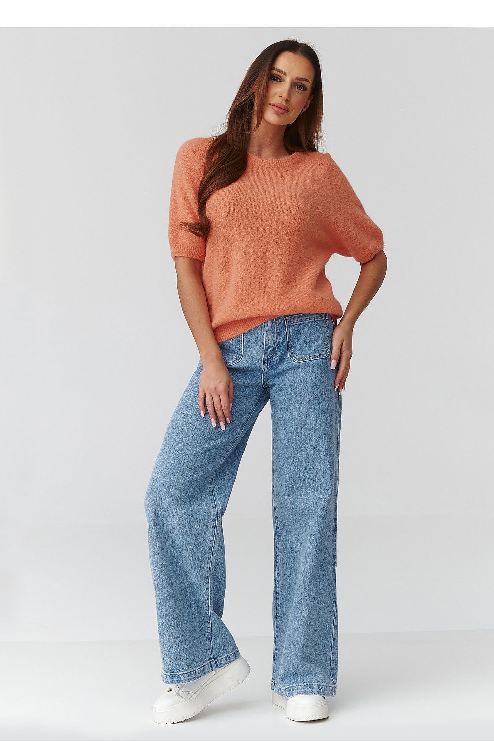 Woman wearing a coral sweater and blue jeans on a white background