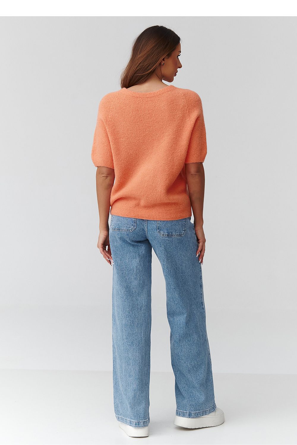 Person wearing an orange sweater and blue jeans on a light gray background