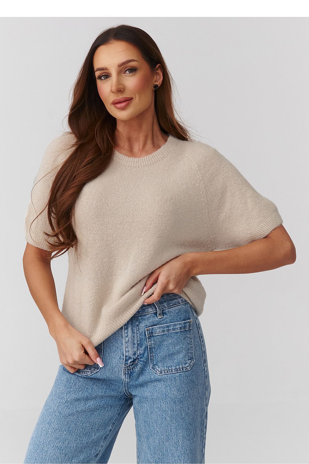 Woman wearing a beige sweater and blue jeans on a plain background