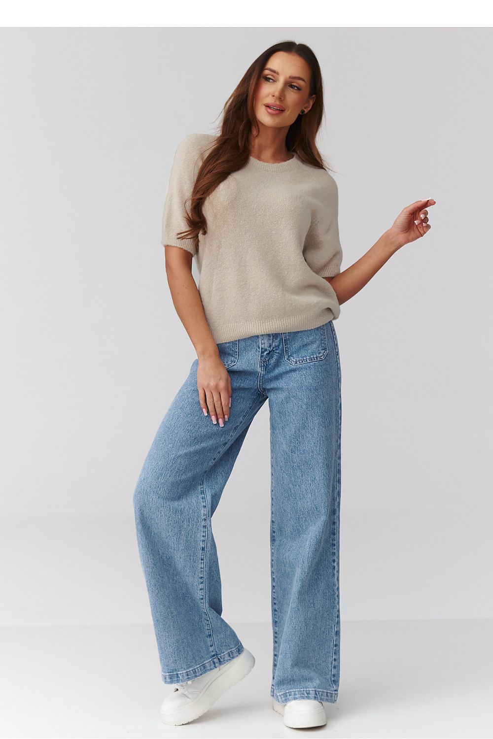 Woman wearing a beige sweater and blue jeans on a white background