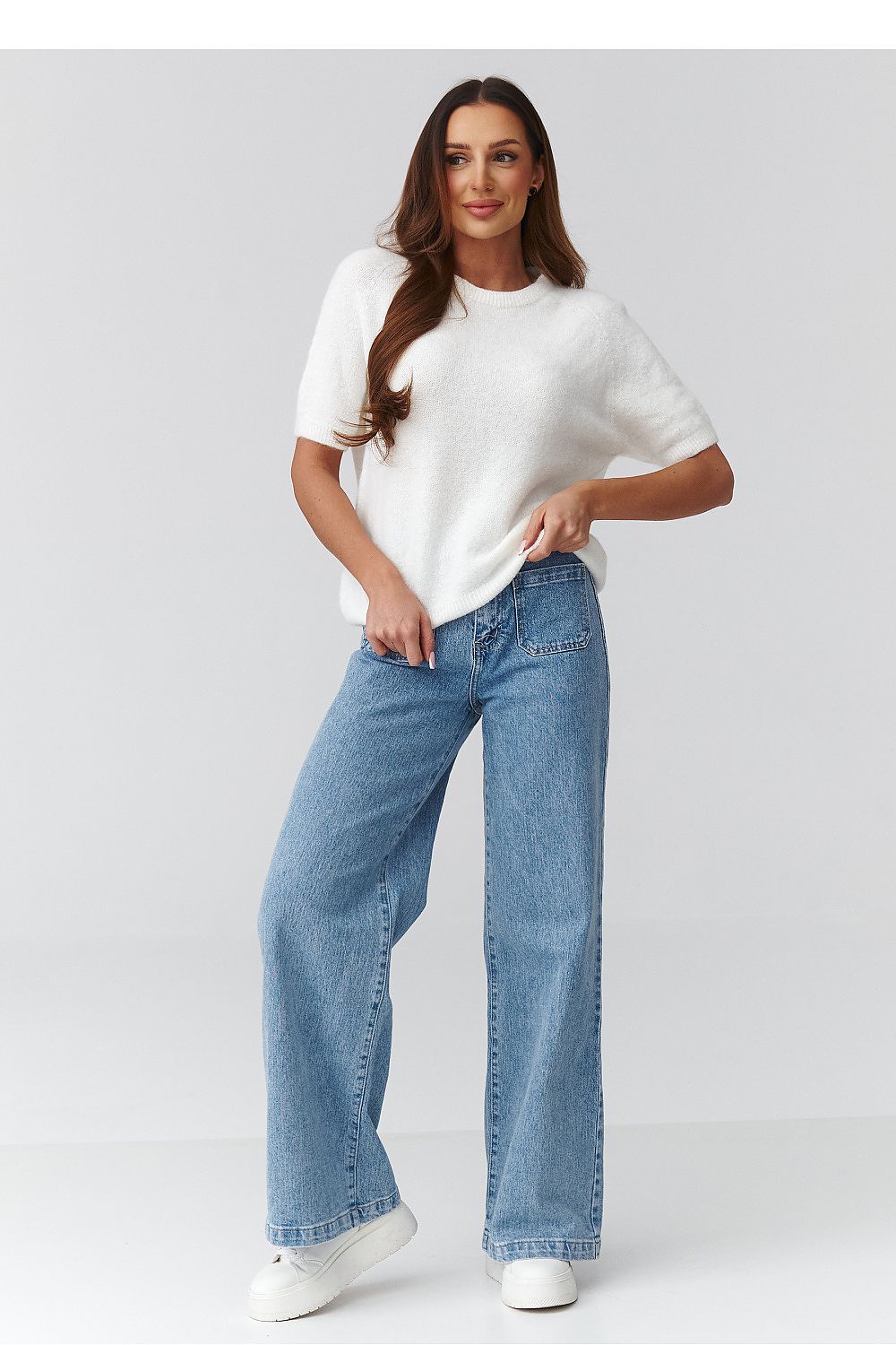 Woman wearing a white t-shirt and blue jeans on a plain background