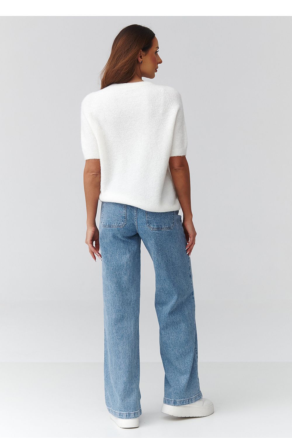 Woman wearing a white top and blue jeans on a plain background