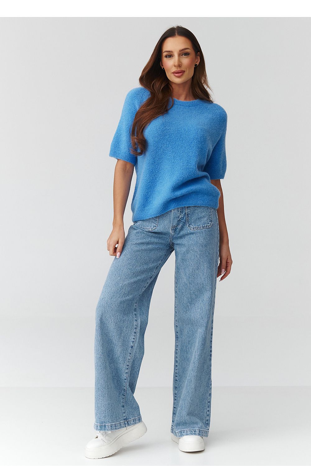 Woman wearing a blue sweater and light blue jeans on a white background