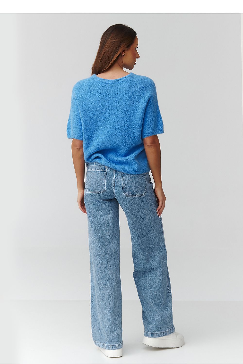 Person wearing a blue sweater and light blue jeans on a white background