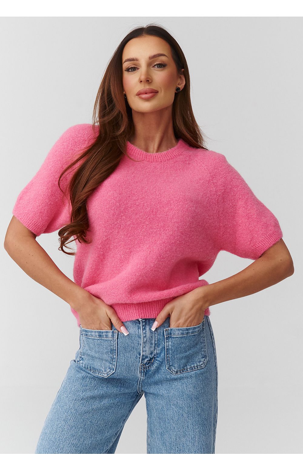 Woman wearing a pink sweater and blue jeans on a light gray background