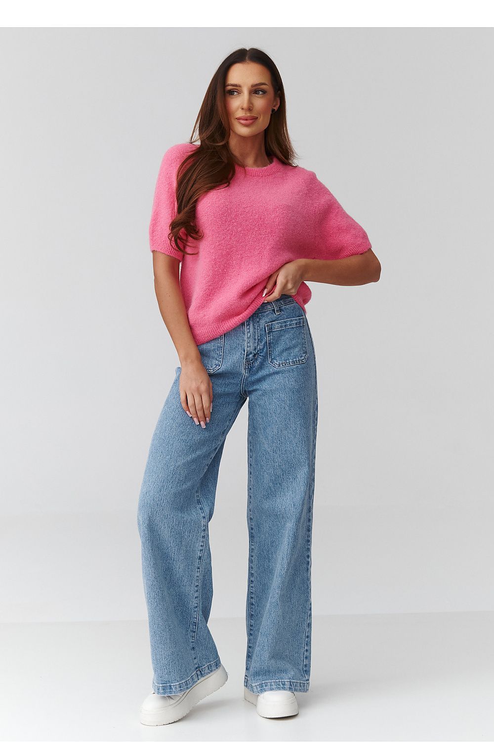 Woman wearing a pink sweater and blue jeans on a white background