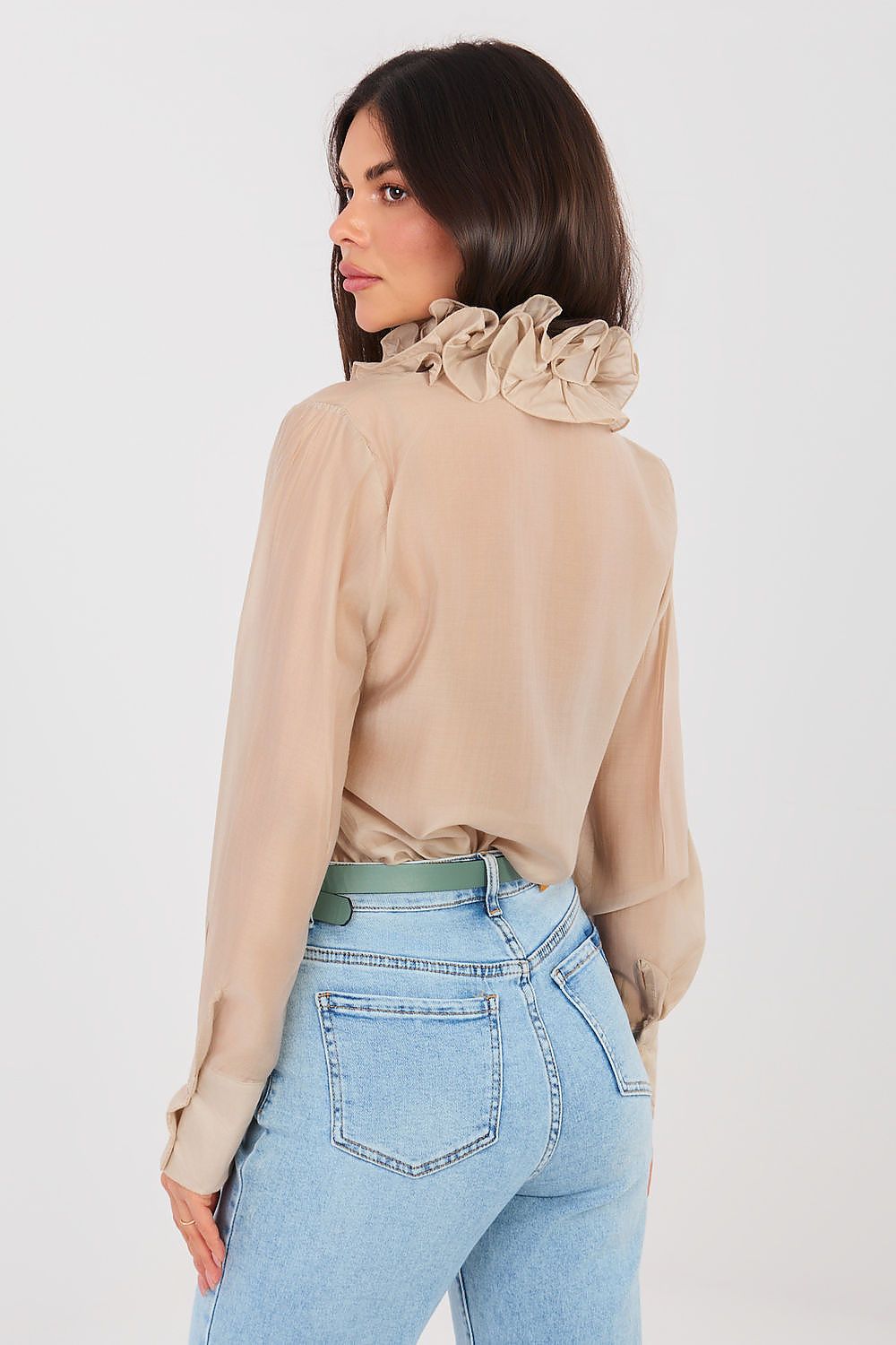 Woman wearing a beige blouse with ruffled details and light blue jeans on a white background