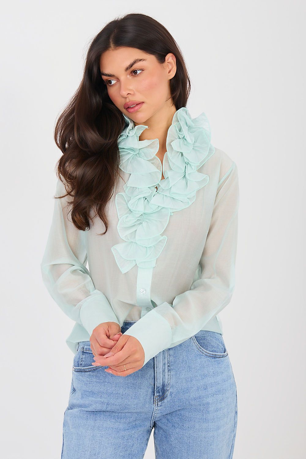 Woman wearing a light green blouse with ruffled details and blue jeans on a white background
