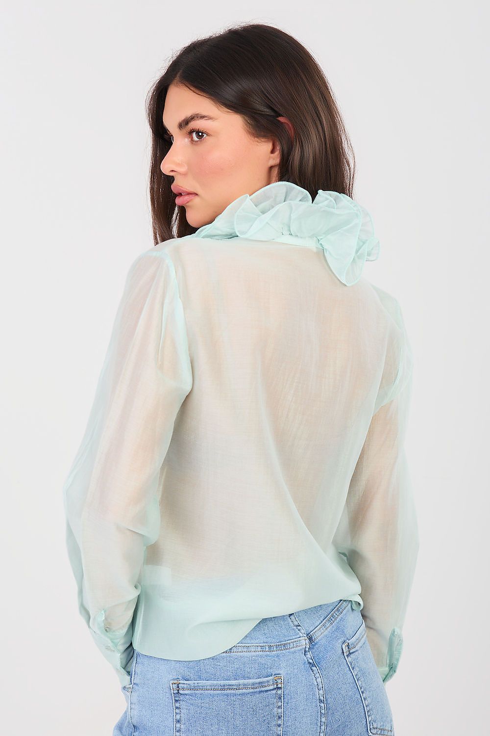 Woman wearing a sheer light green blouse over a solid color top with blue jeans on a white background