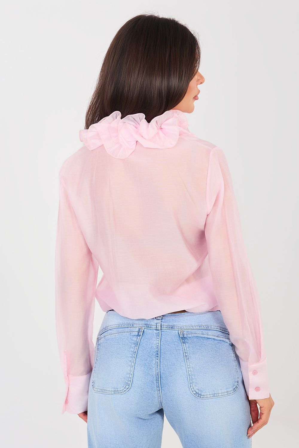 Woman wearing a pink ruffled blouse and light blue jeans against a plain background