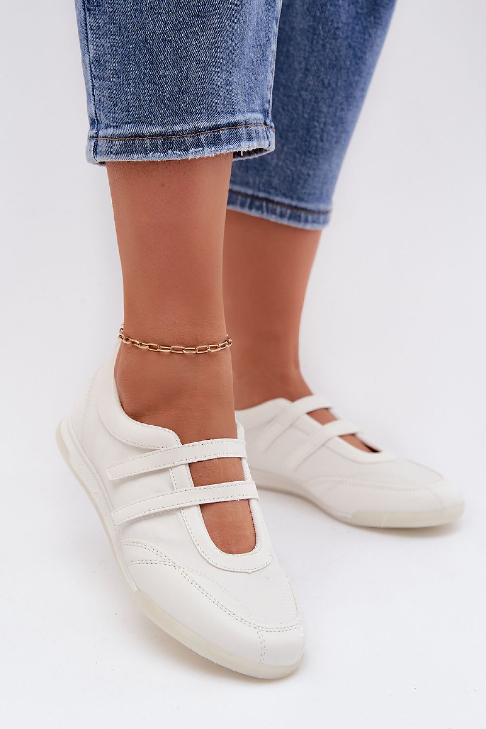 White flat shoes worn with blue jeans on a white background