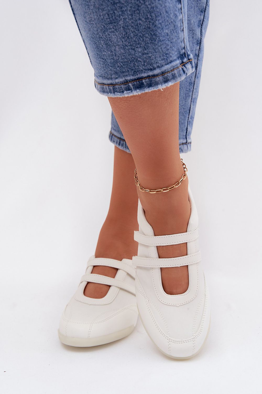 White flat shoes worn with rolled-up jeans on a white background