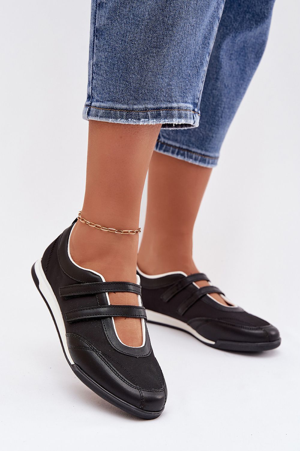 Black shoes with white soles worn with blue jeans on a white background