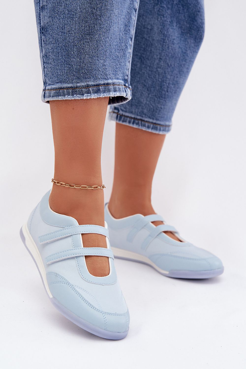 Light blue flat shoes worn with rolled-up jeans on a white background