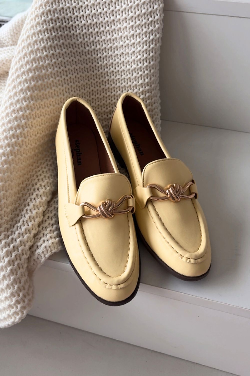 Pair of beige loafers with gold accents on a light surface.
