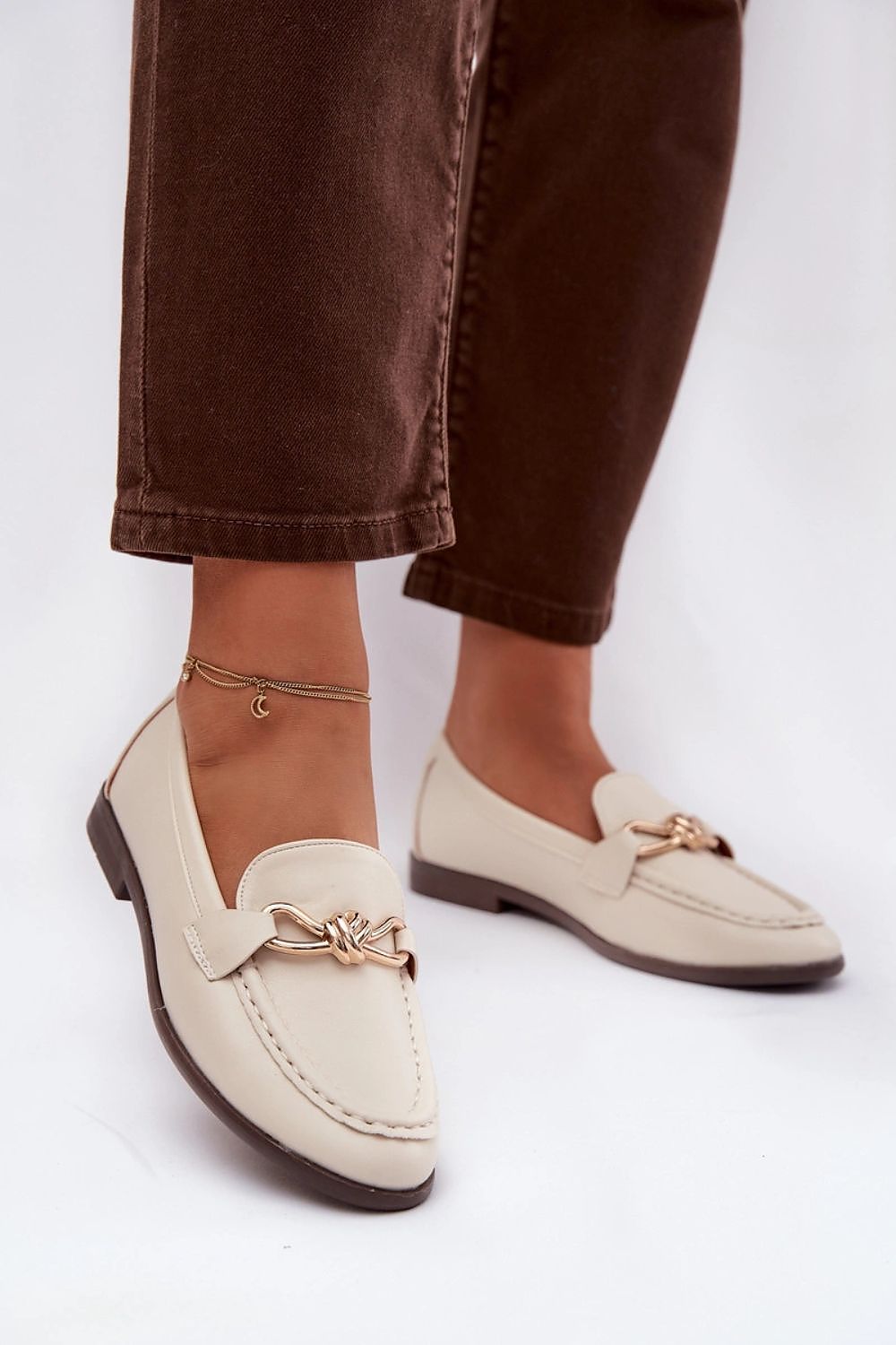 Beige loafers worn with brown pants on a white background