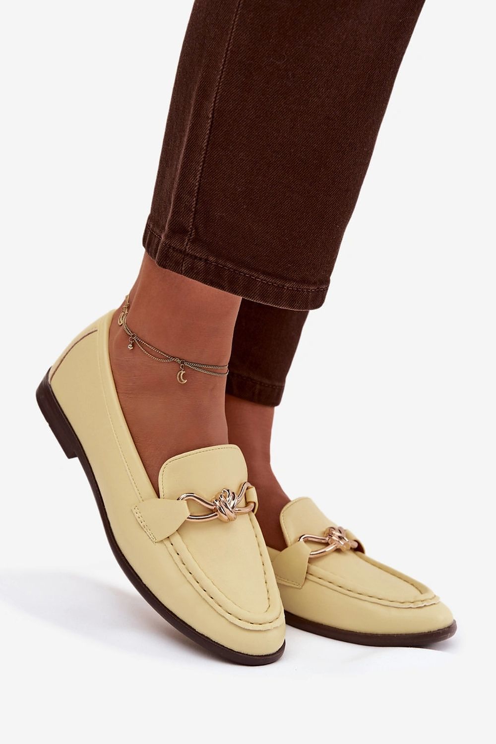 Beige loafers with gold accents worn by a person on a white background