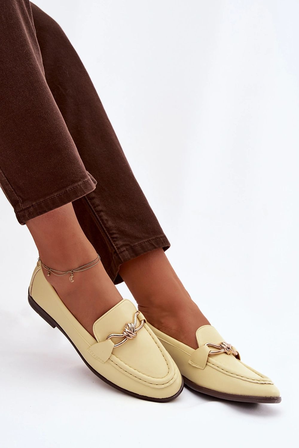 Yellow loafers worn with brown pants on a white background