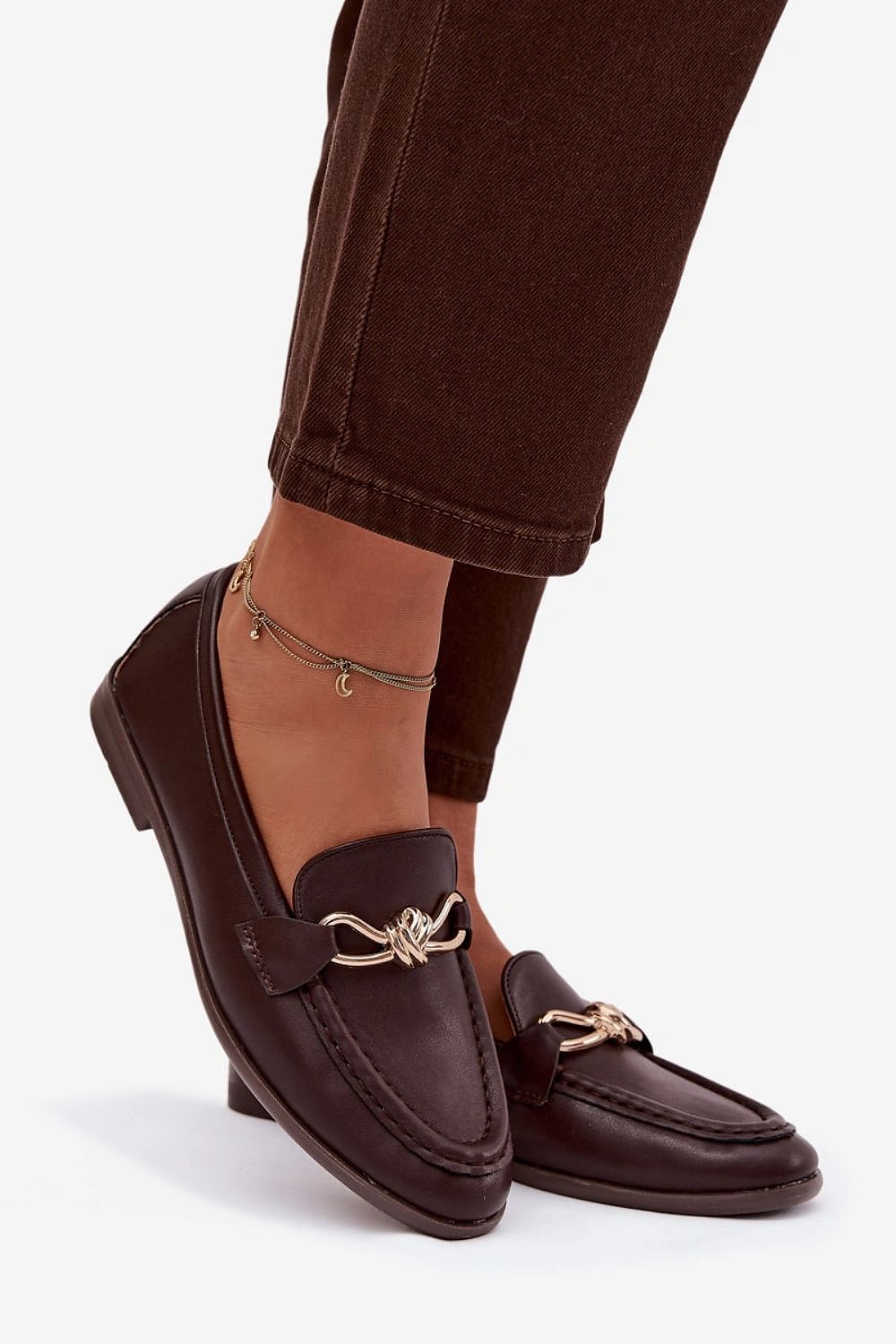 Brown loafers with gold accents worn with brown pants on a white background