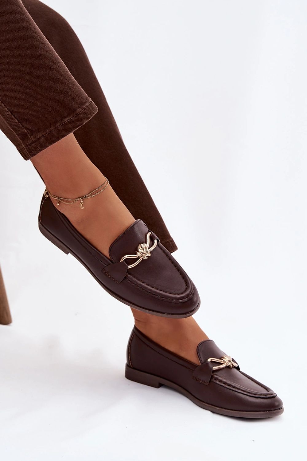 Brown loafers with decorative straps worn by a person on a white background