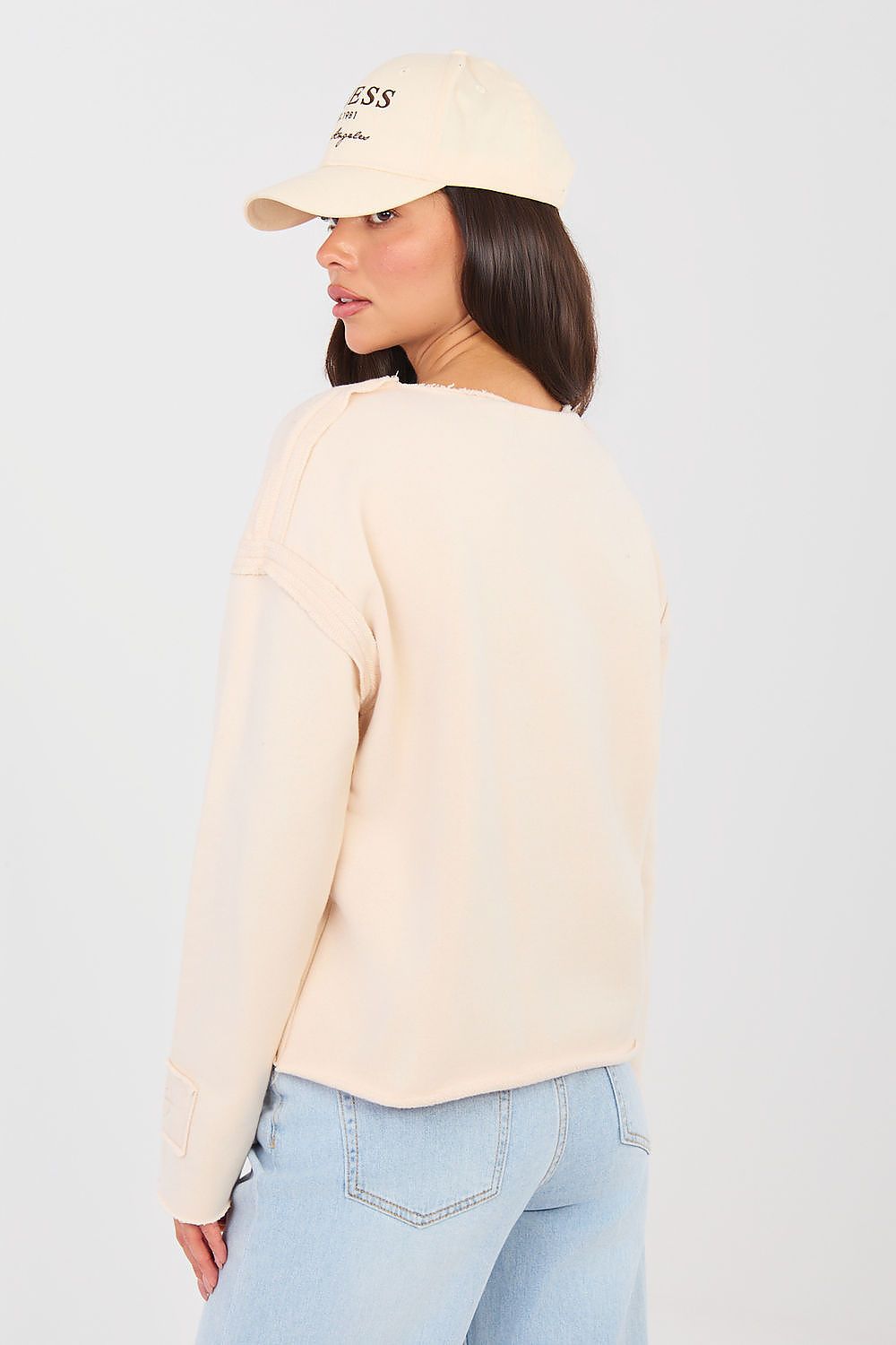 Woman wearing a beige cap and sweater with light blue jeans on a plain background