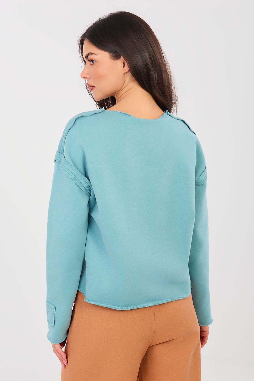 Woman wearing a light blue sweater and brown pants on a white background
